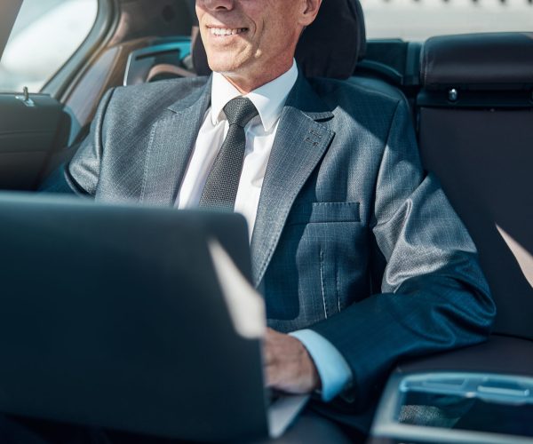 Cropped head of happy businessman using notebook while being transported by driver after landing in airport